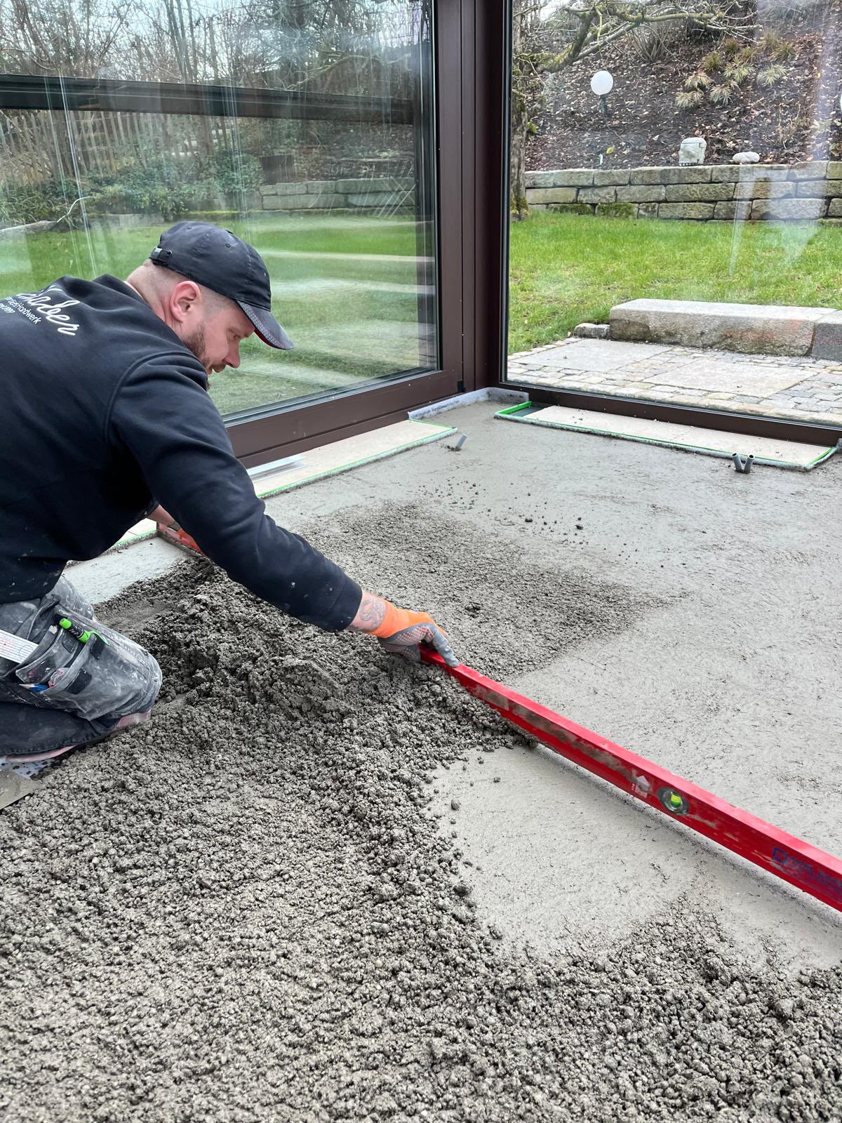 Fliesenleger beim Glätten des frischen Estrichs mit einer Richtlatte