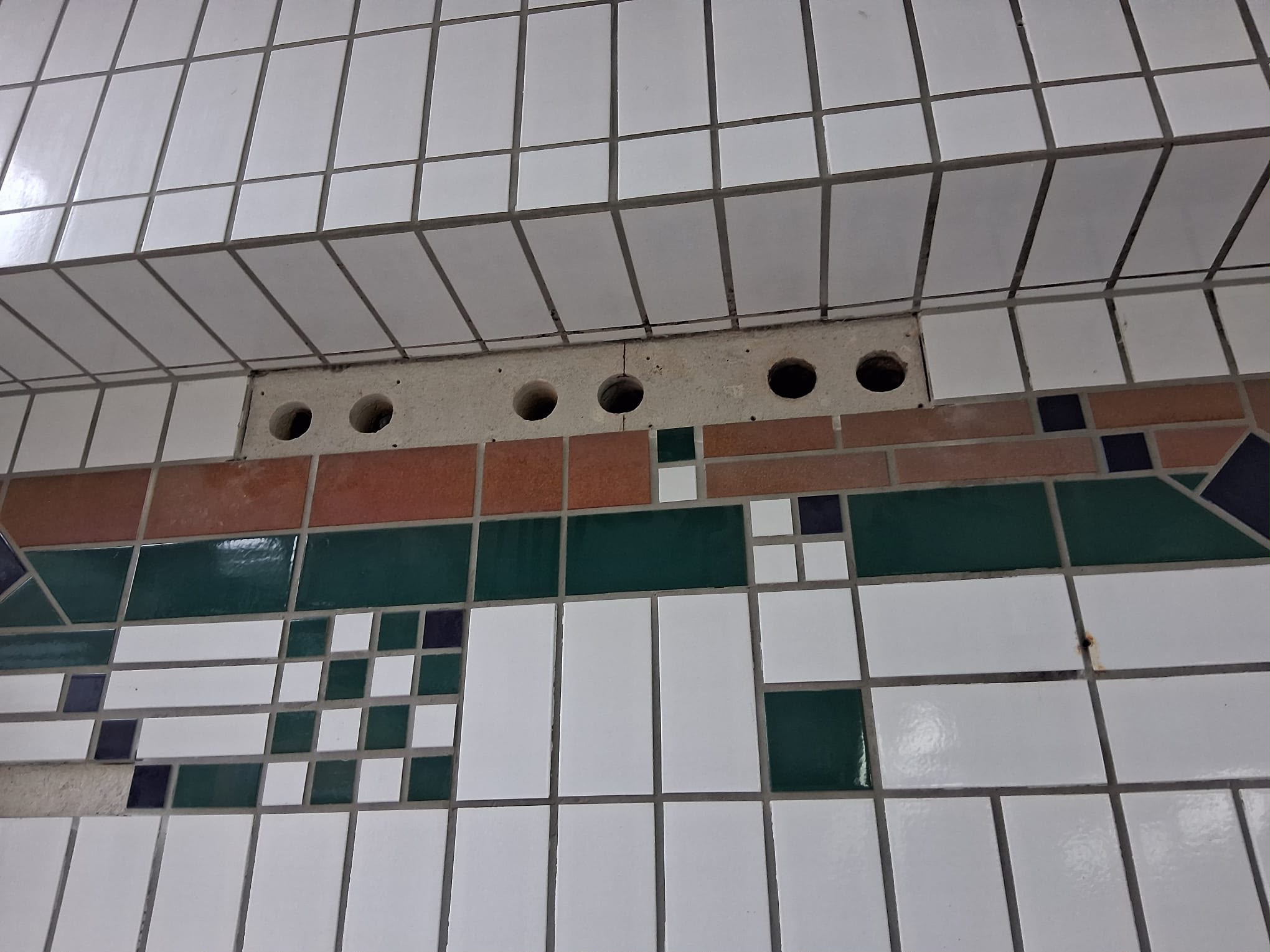Detailaufnahme einer gefliesten Wand mit weißen und grünen Fliesen sowie offenen Bohrlöchern