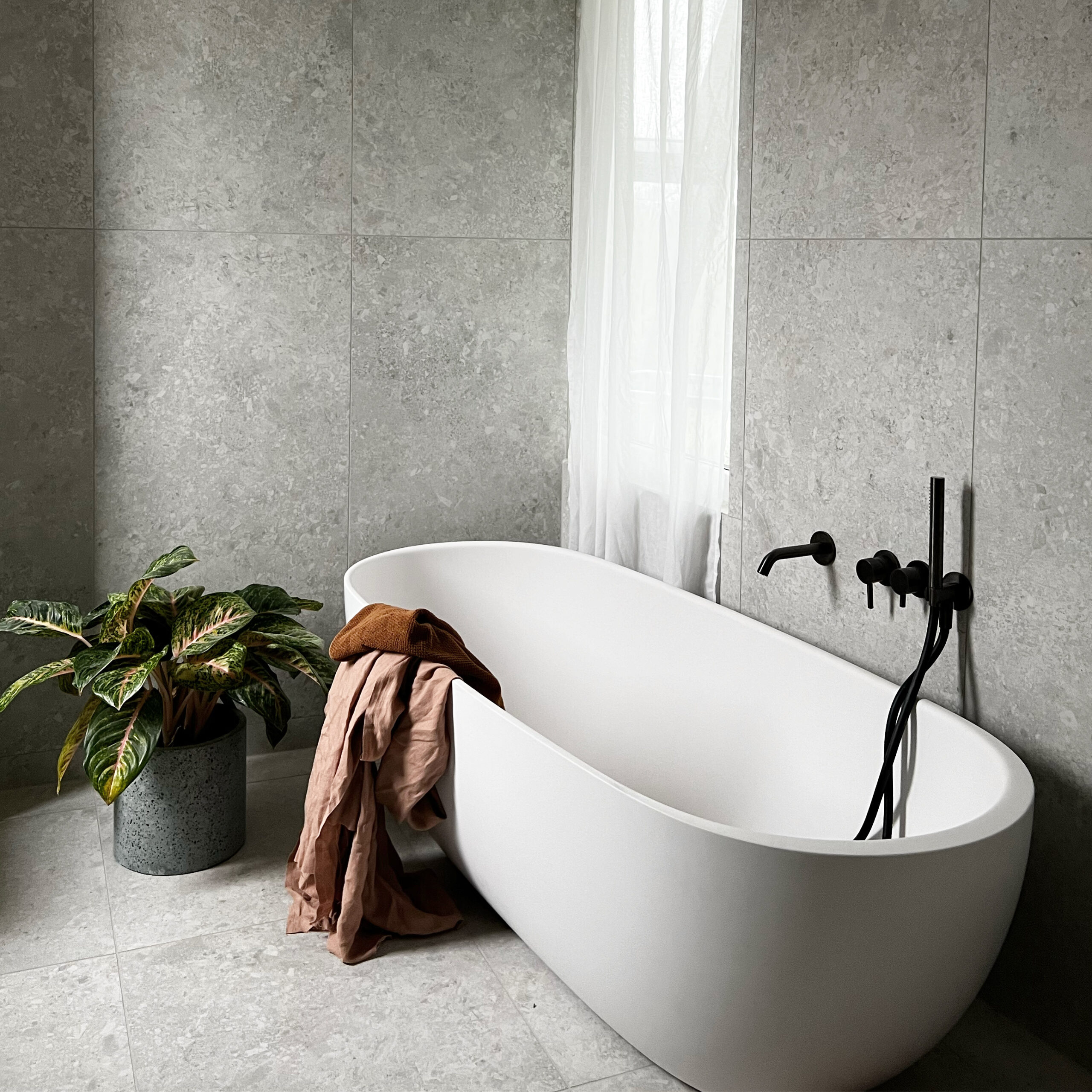 Modernes Badezimmer mit freistehender Badewanne und grauen Fliesen in Betonoptik
