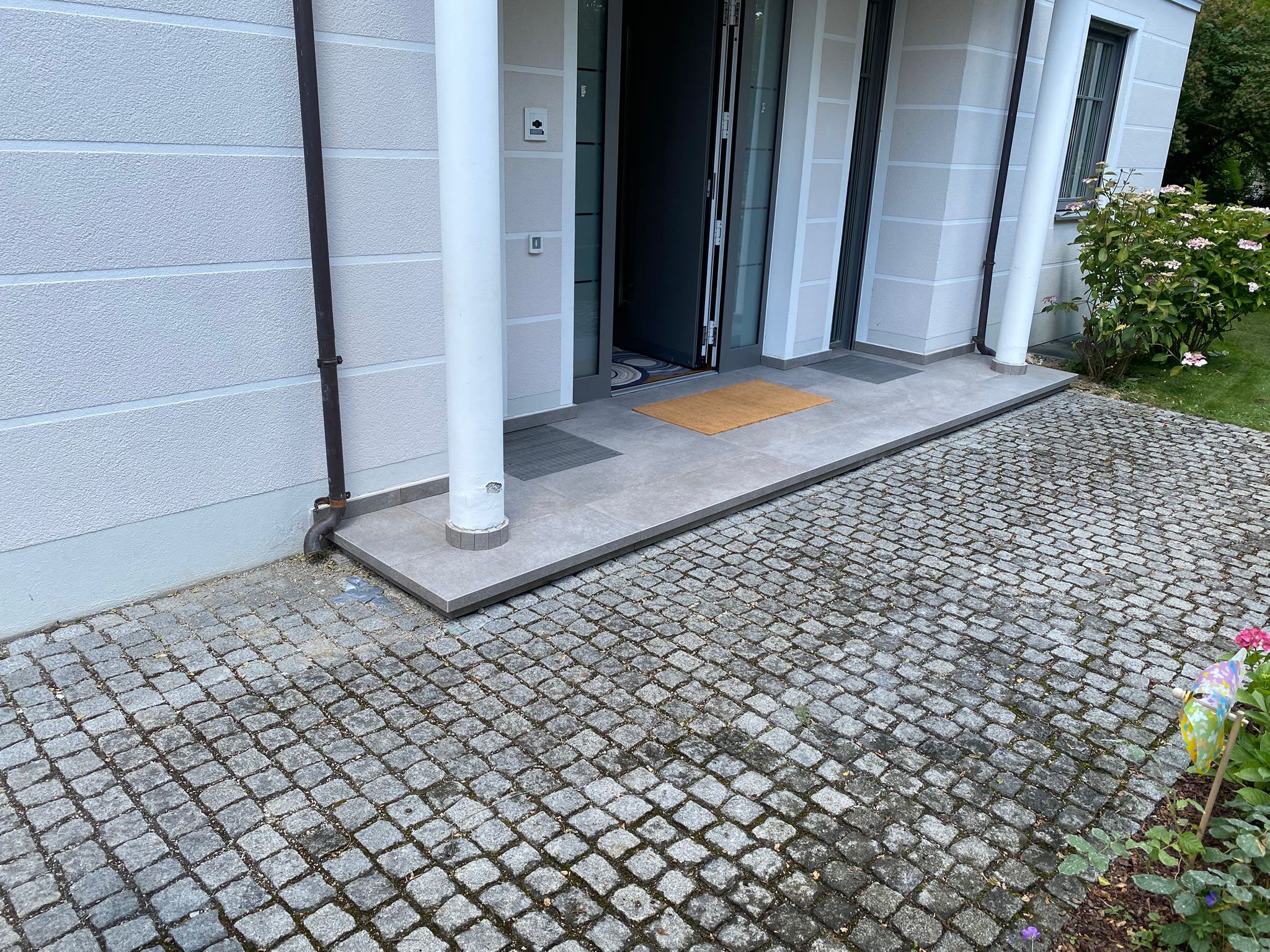 Hauseingang mit Natursteinpflaster und grauen Bodenplatten