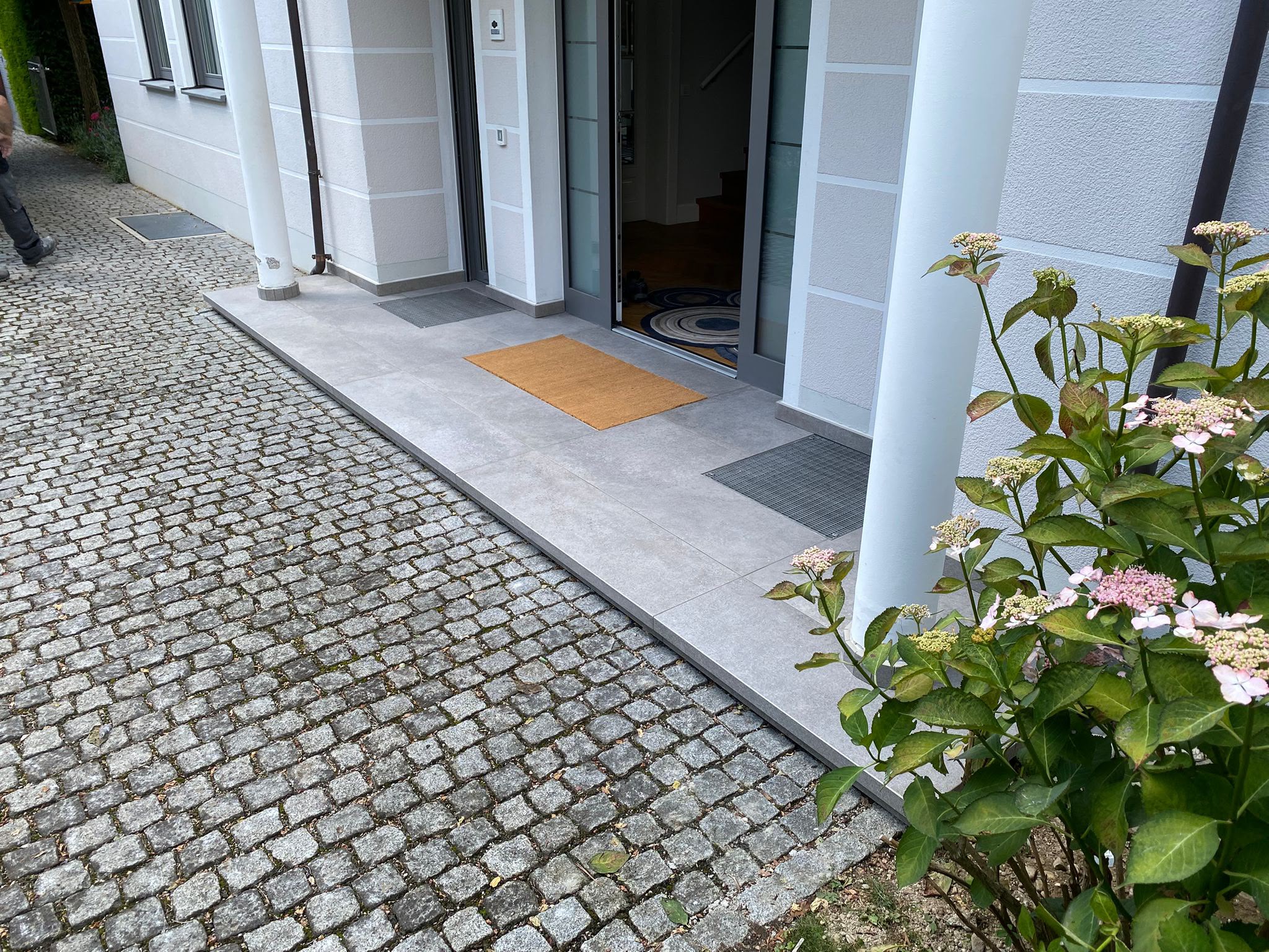 Gepflasterter Eingangsbereich mit grauen Bodenplatten und Natursteinpflaster