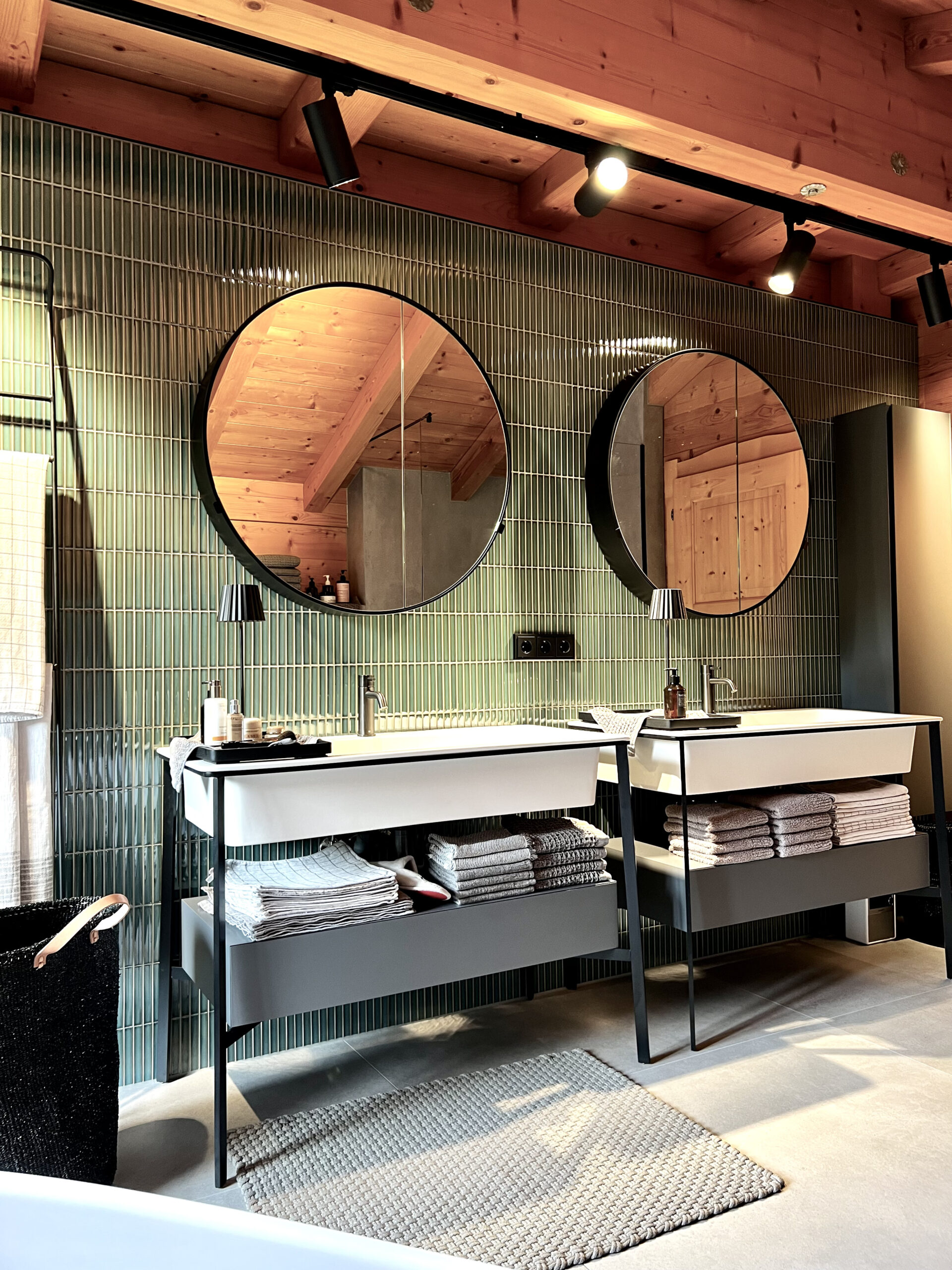 Badezimmer mit grünen Fliesen im Hochformat, Waschbecken und rundem Spiegel