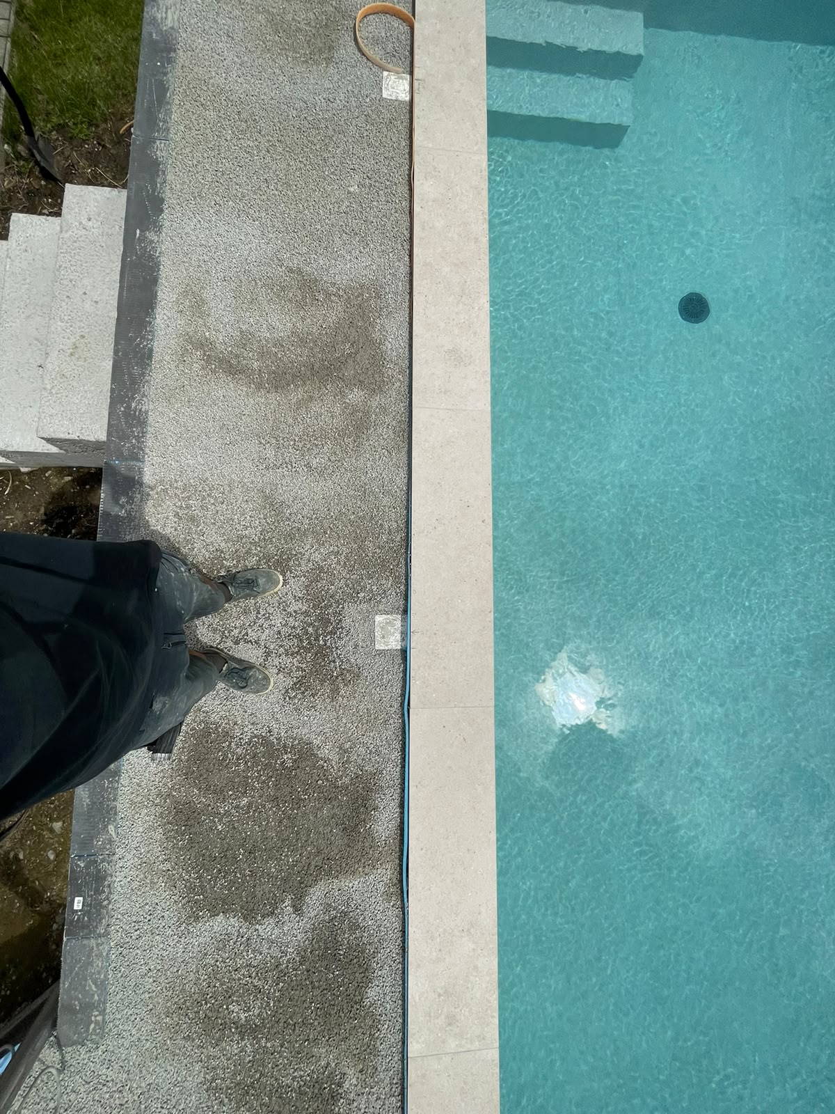 Detailaufnahme eines Poolrands mit grauem Natursteinbelag und türkisfarbenem Wasser