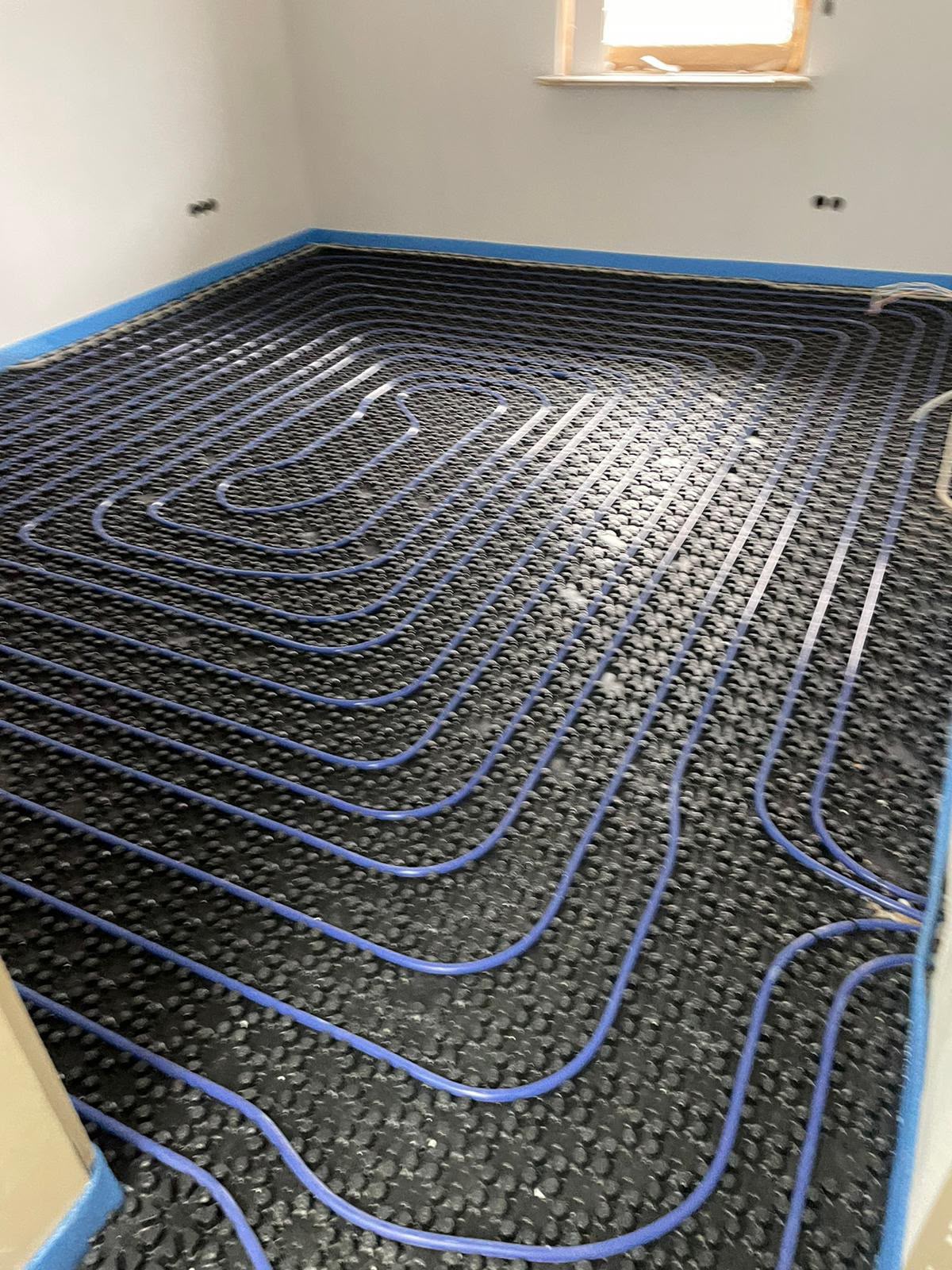 Verlegte Fußbodenheizung mit blauen Heizrohren auf schwarzen Noppenplatten